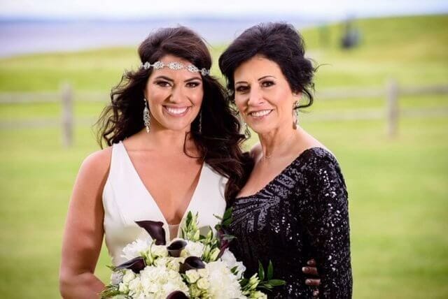 A bride and her mother posing outside with green grass behind them.