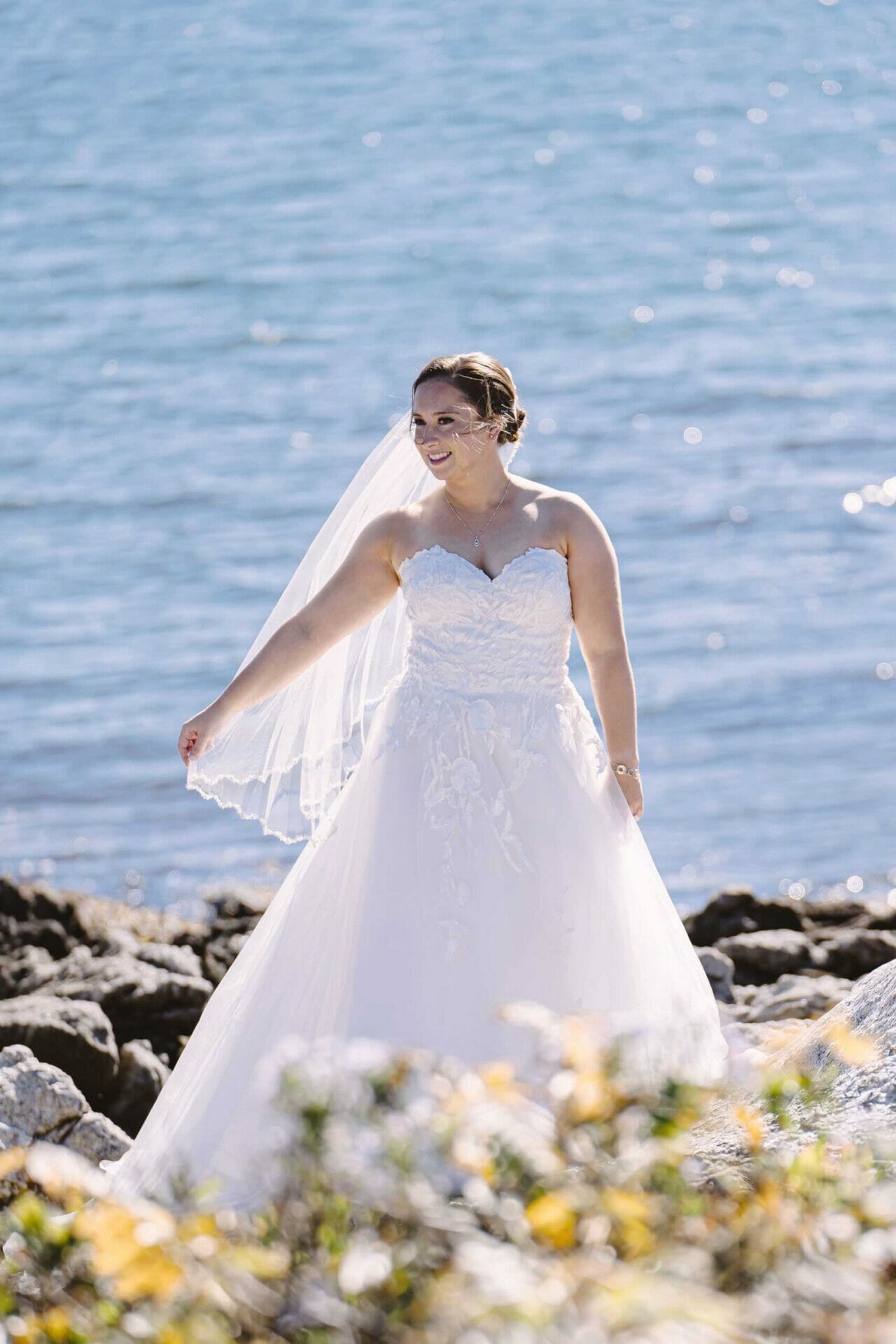A bride in a wedding dress standing on rocks near the water, showcasing the elegance of bridal couture.