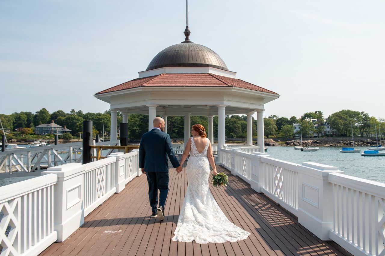 A bride and groom enjoying a romantic stroll on a pier near a gazebo, envisioning their dream wedding and the beautiful wedding dresses they'll find at a nearby bridal store or bridal shop.