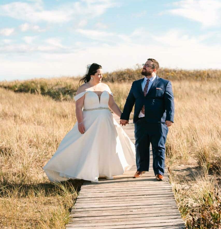 A bride and groom walking on a wooden boardwalk in their wedding attire.