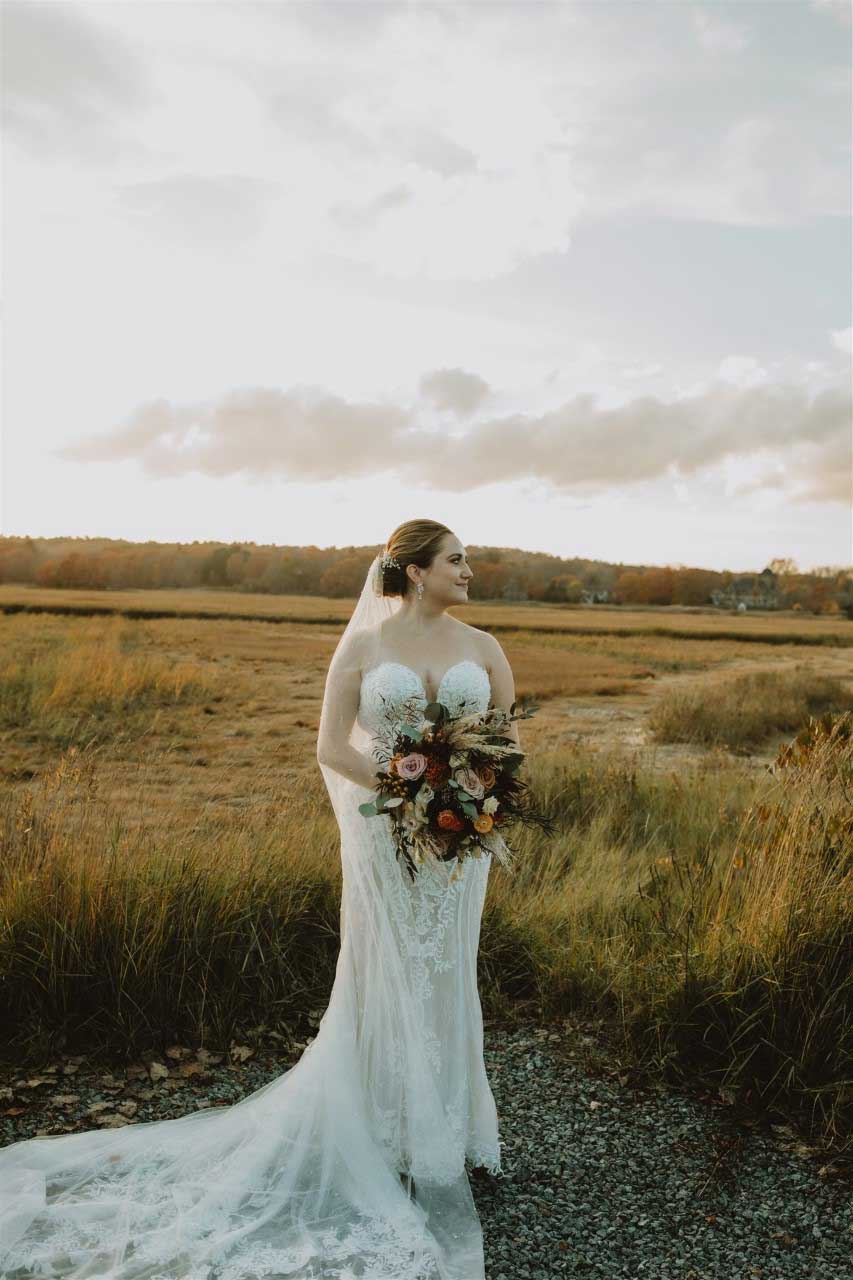 A bride standing in a field with her wedding bouquet, showcasing the elegant beauty of wedding dresses.