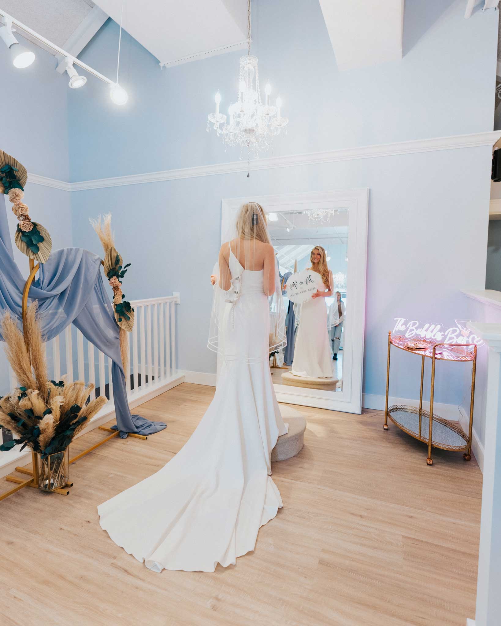 about-bella-sera-bride-says-yes A bride in a wedding dress standing in front of a mirror at a bridal store.