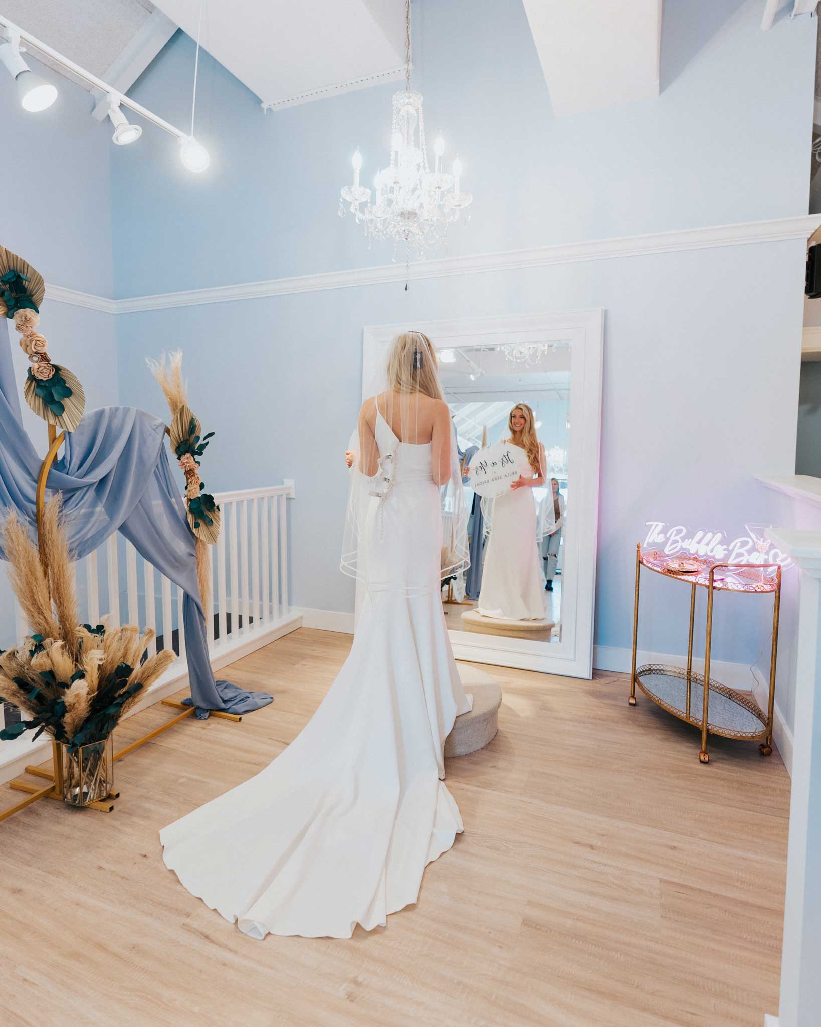 A bride in a wedding dress standing in front of a mirror at a bridal store.