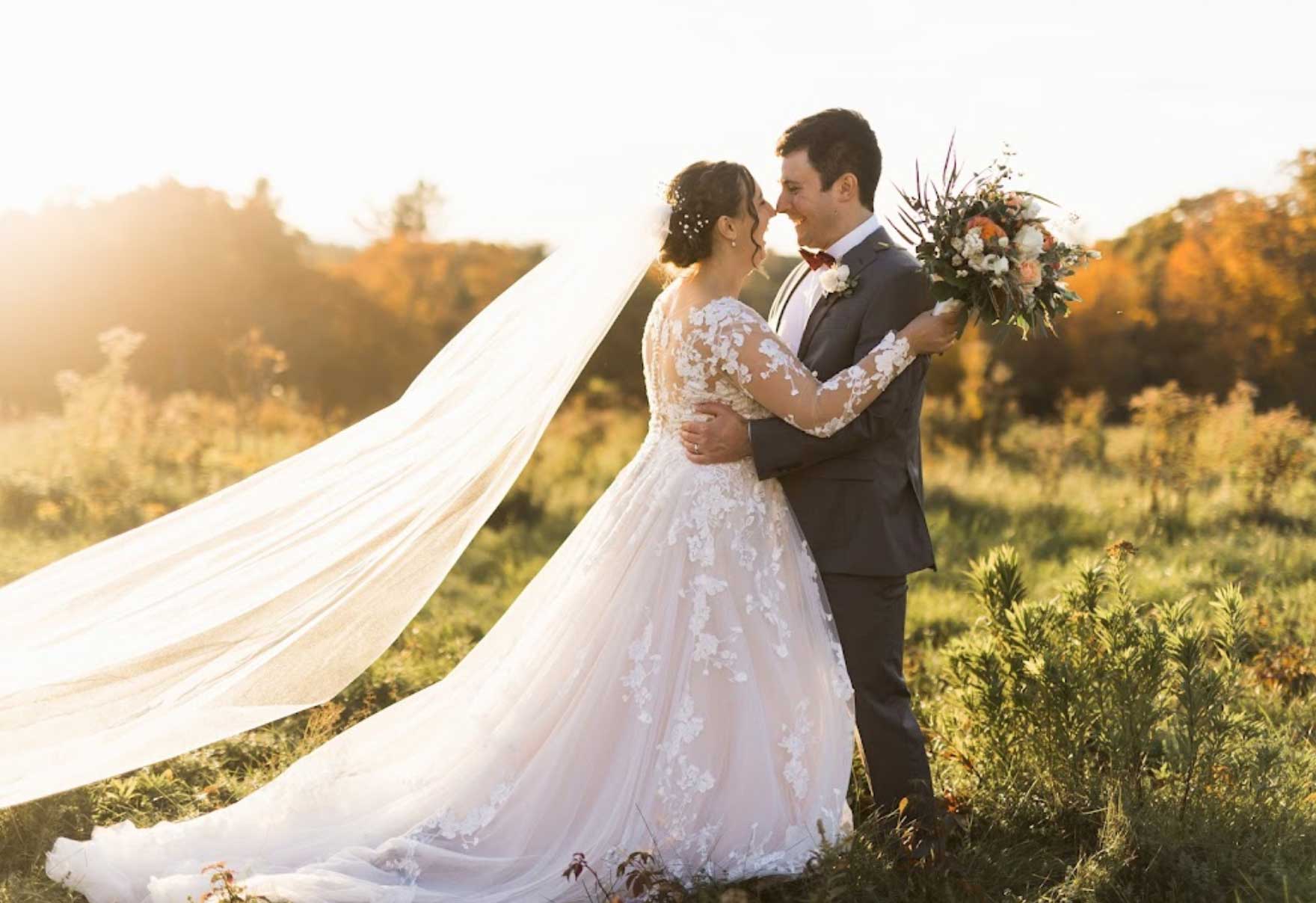 custom-alternations-wedding-dresses A bride and groom embrace in a field at sunset, capturing the essence of their special day.