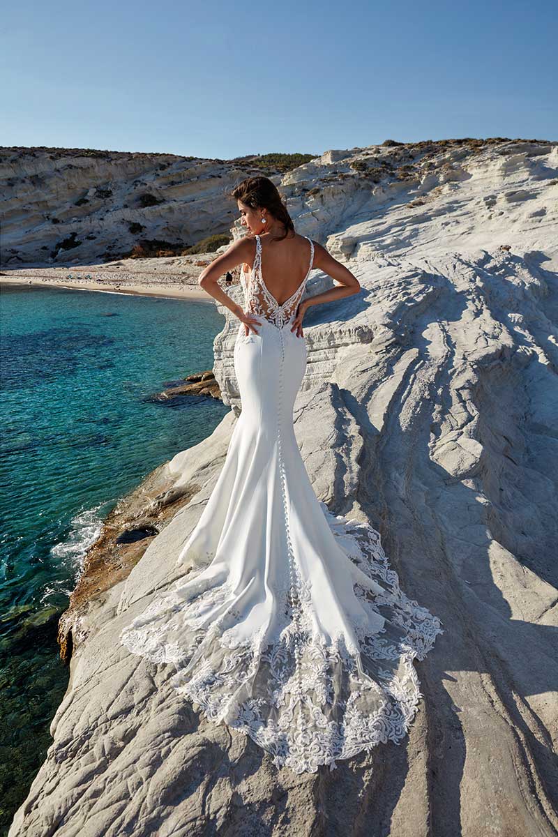 A woman in a white wedding dress is standing on a rocky beach, looking elegant and beautiful.