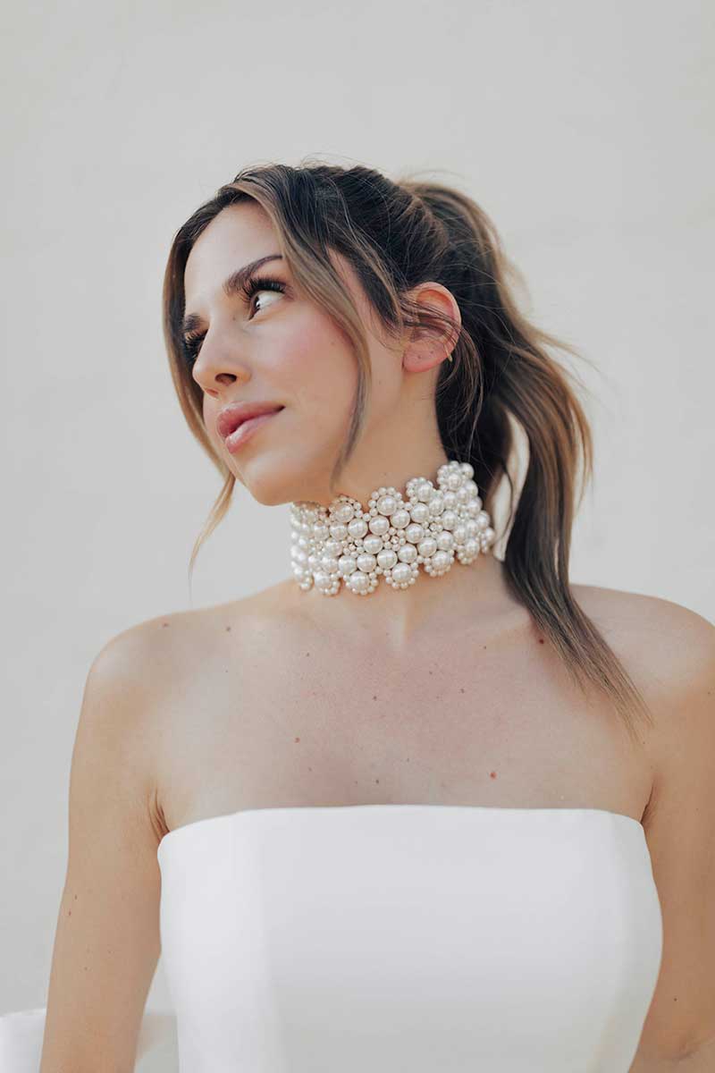A bride-to-be in a white dress beautifully showcases a pearl choker at a bridal store.