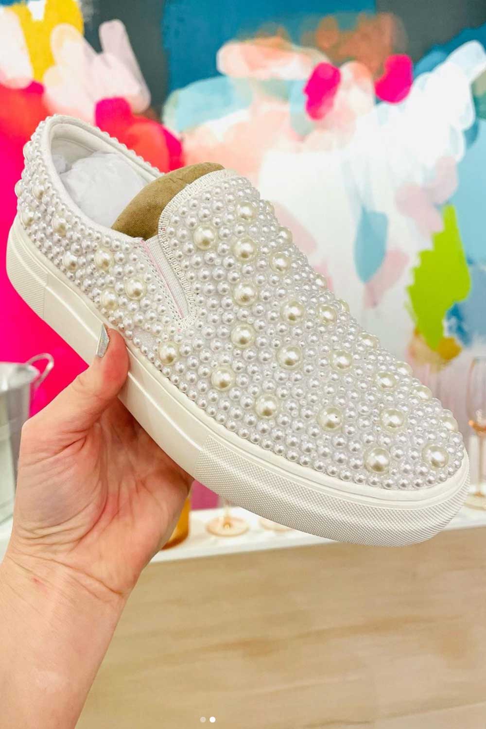 A person showcasing a pair of pearl slip on sneakers in a bridal store.