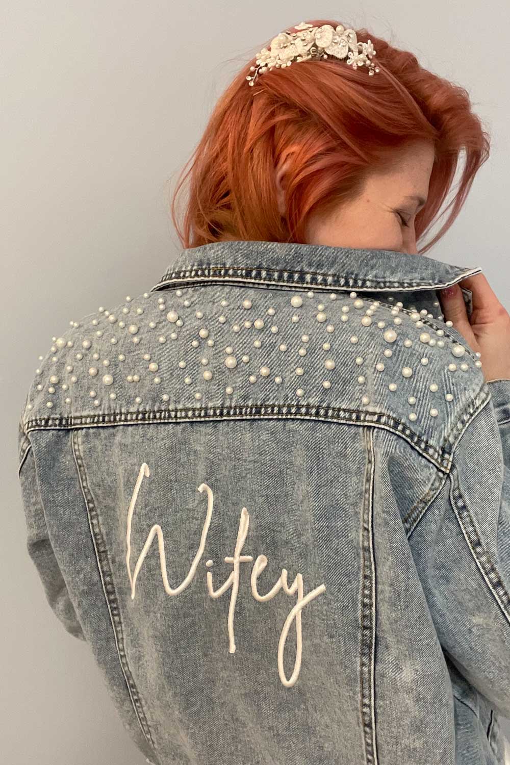 A woman wearing a denim jacket with the word wifey on it, walking into a bridal salon.