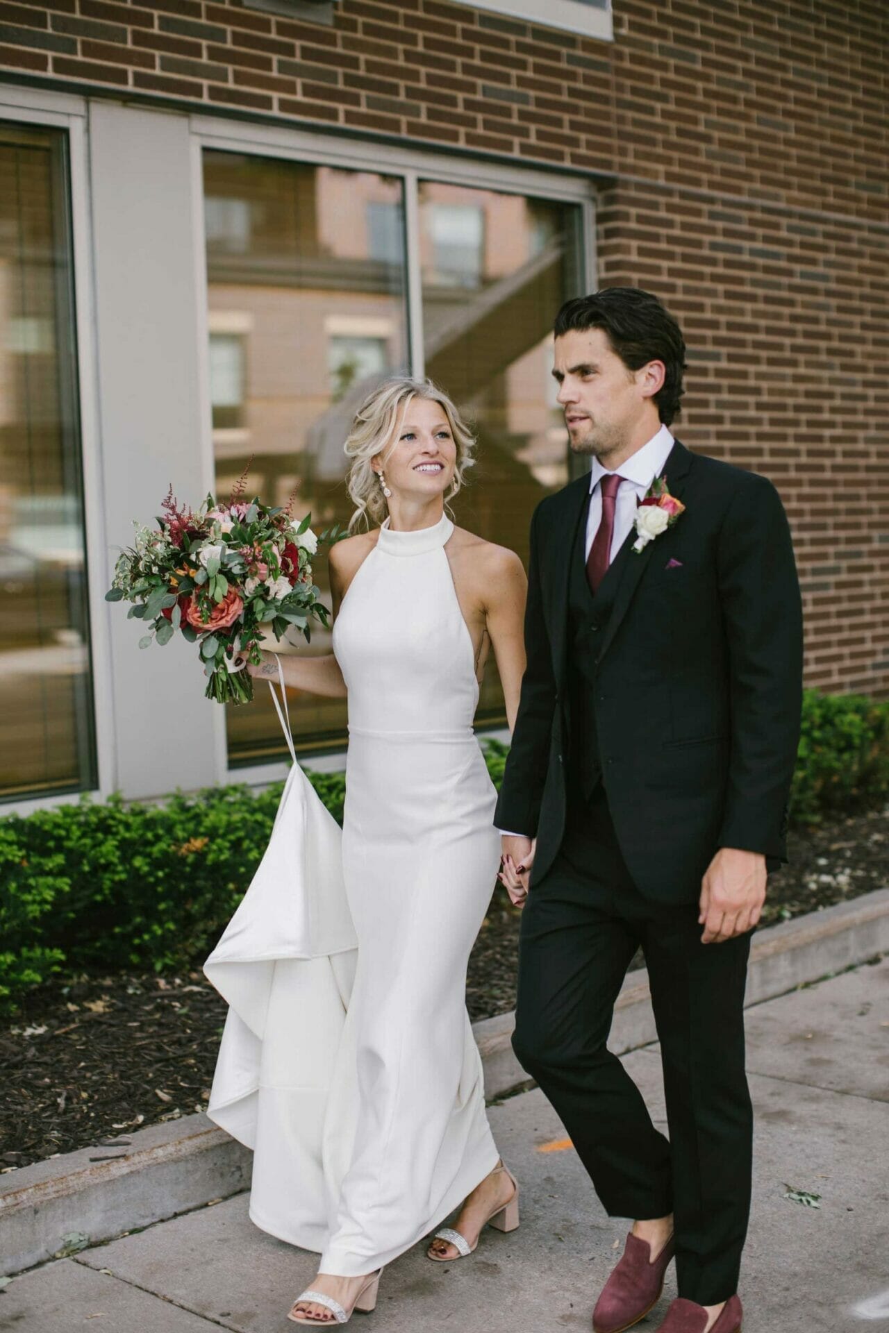 A stunning bride and handsome groom walking down the street, hand in hand, in front of a bridal store.