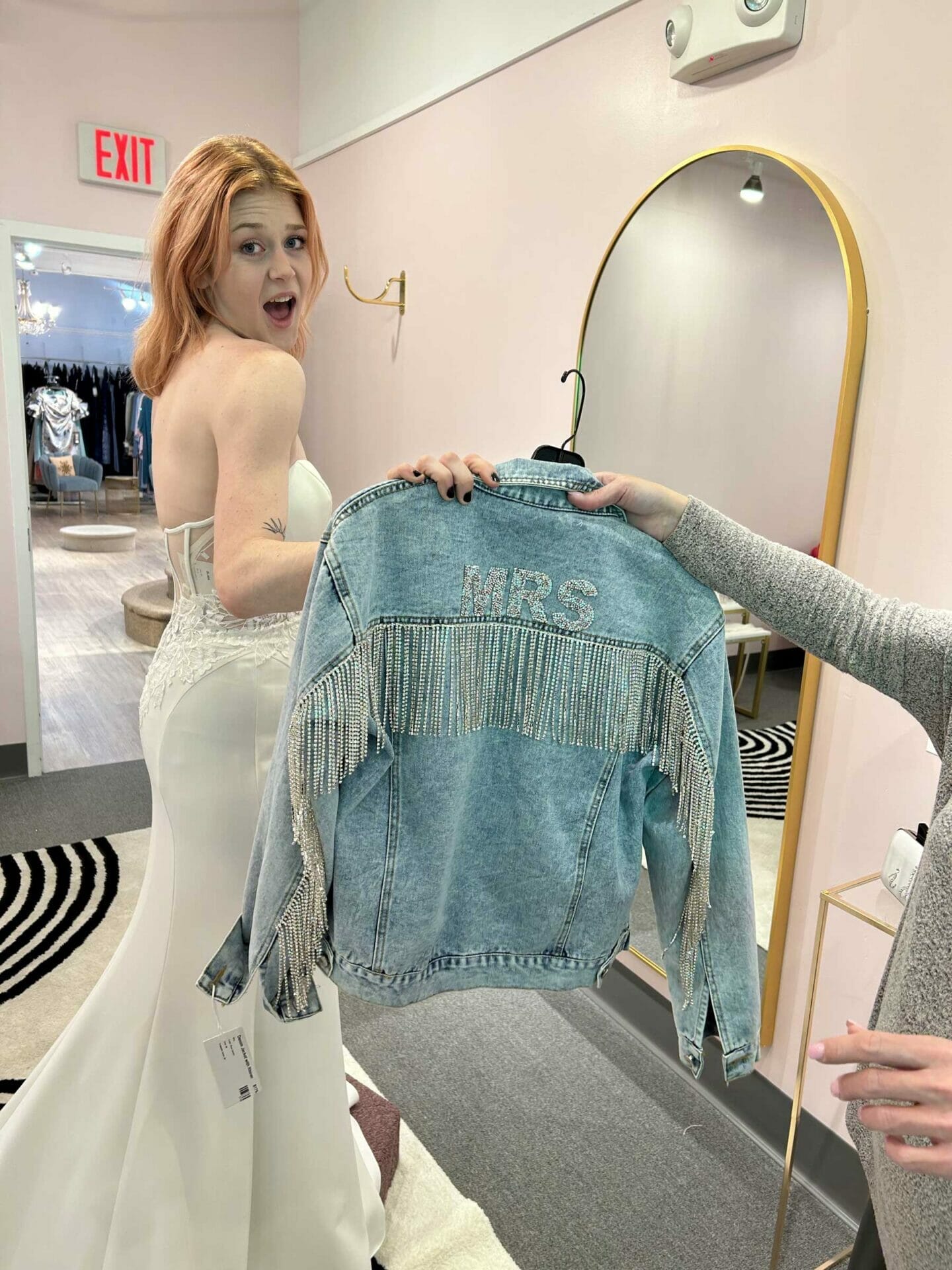 A woman in a wedding dress is looking at a denim jacket in a bridal store.