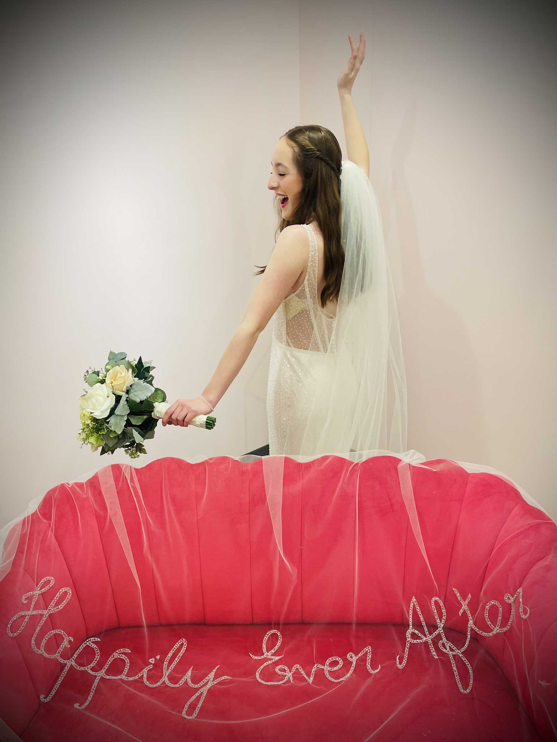 A bride in a wedding dress standing on top of a pink couch in a bridal shop.