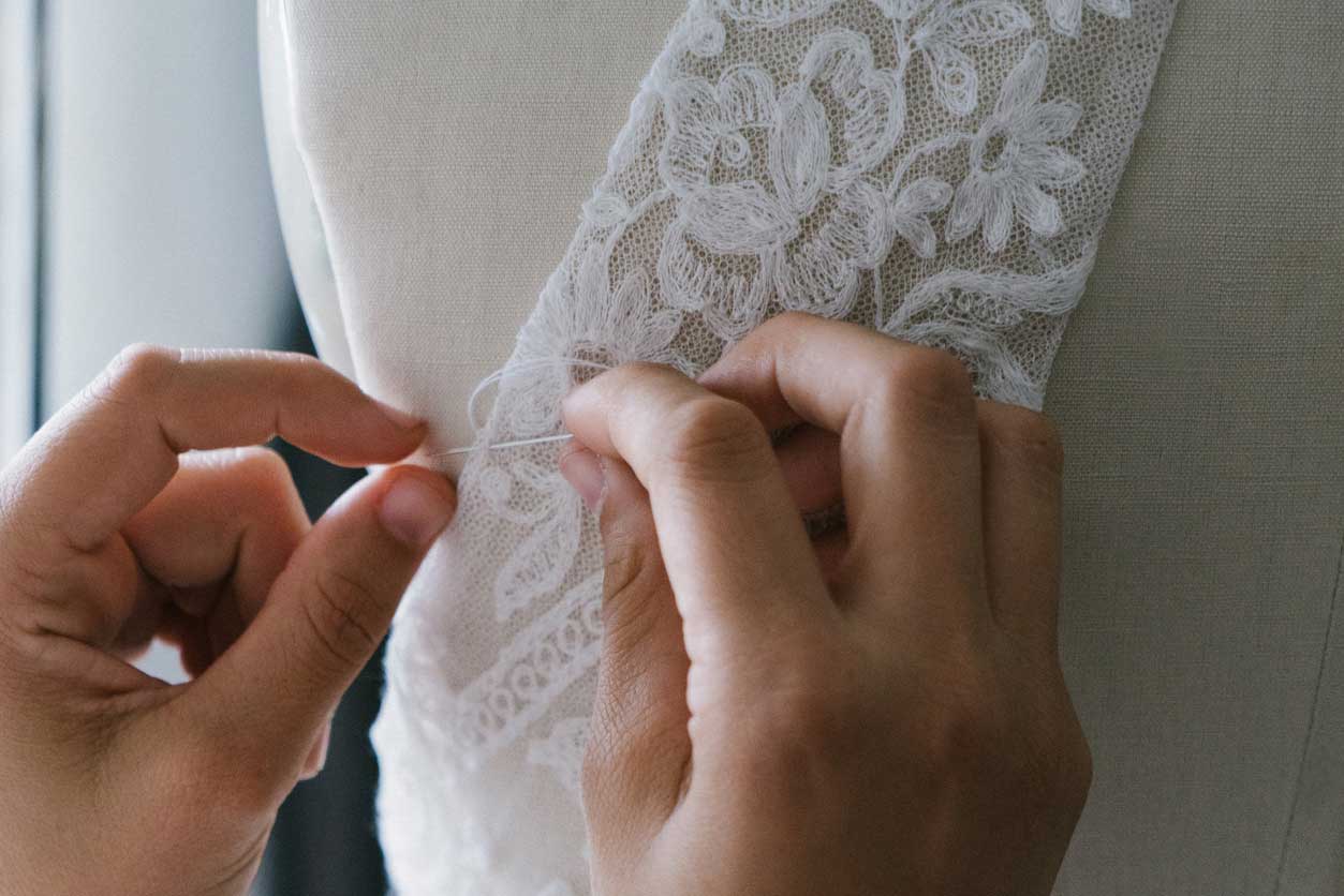 A person is embellishing a wedding dress with lace at a bridal salon.