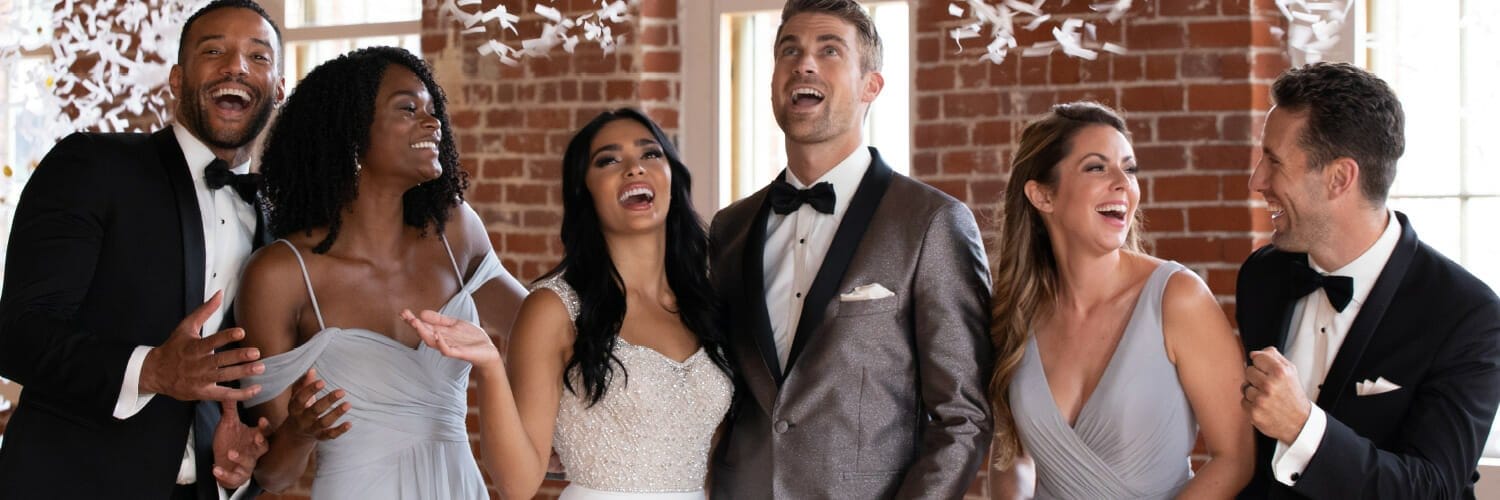 A group of people in wedding dresses and tuxedos are laughing.