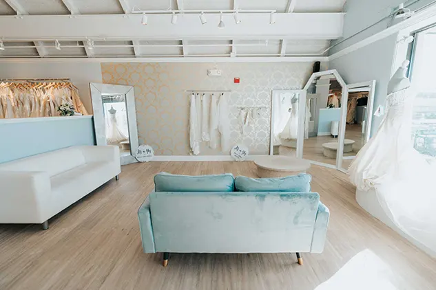 A bridal salon with a blue couch and a mirror.