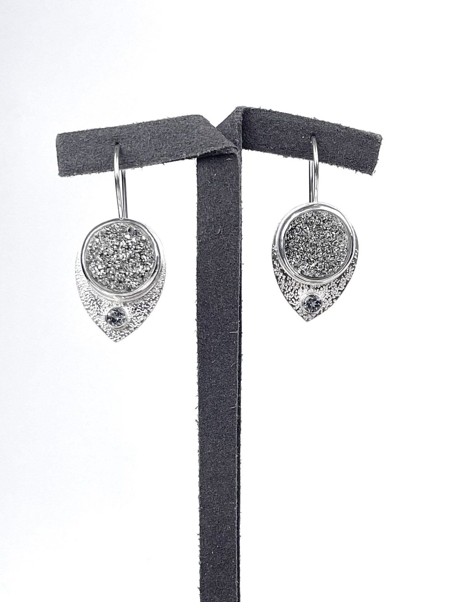 Silver drop earrings with a textured glittery surface, displayed on a gray stand against a white background.