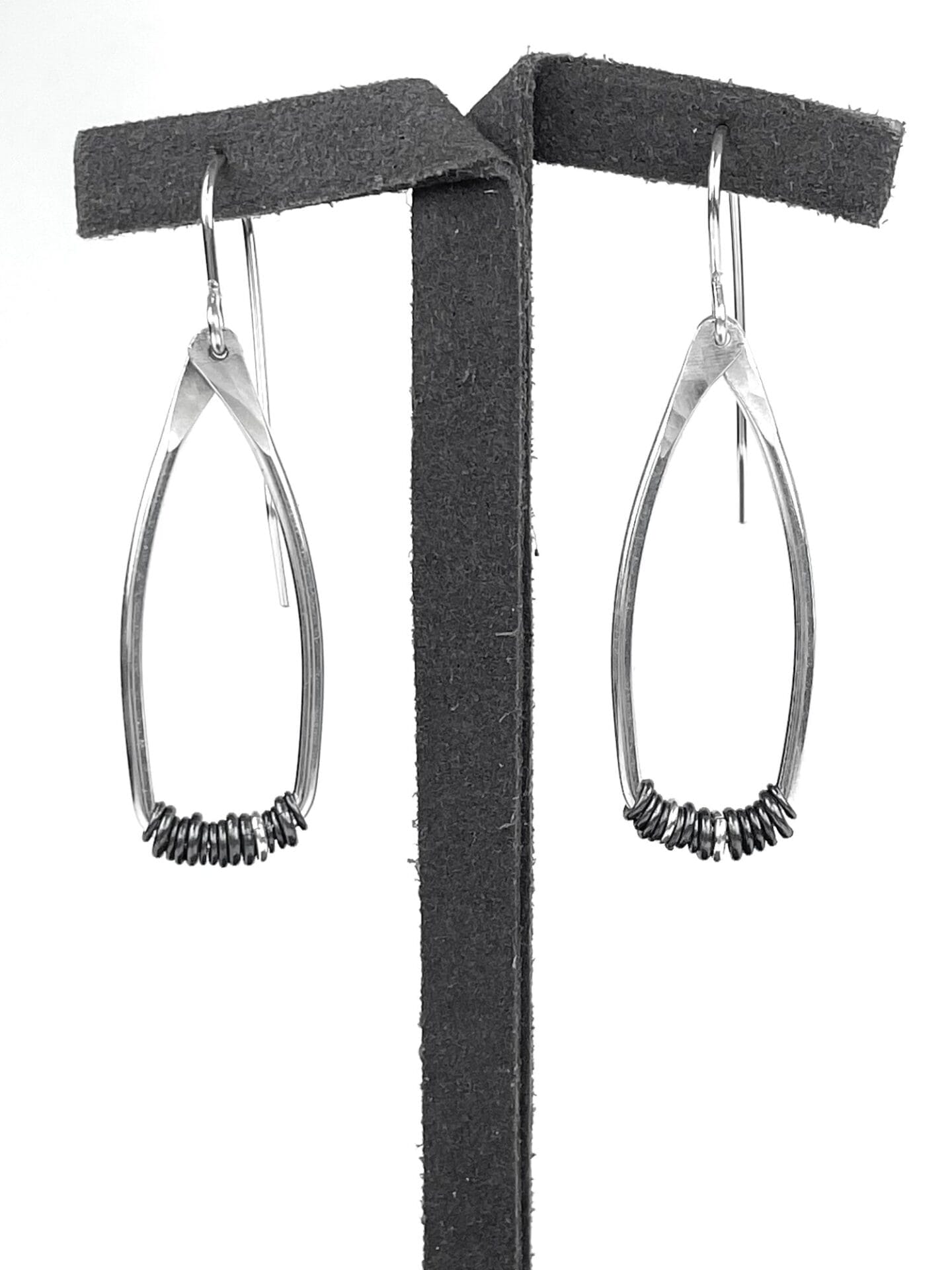 Silver teardrop-shaped earrings with small circular accents, displayed on a black stand against a white background.