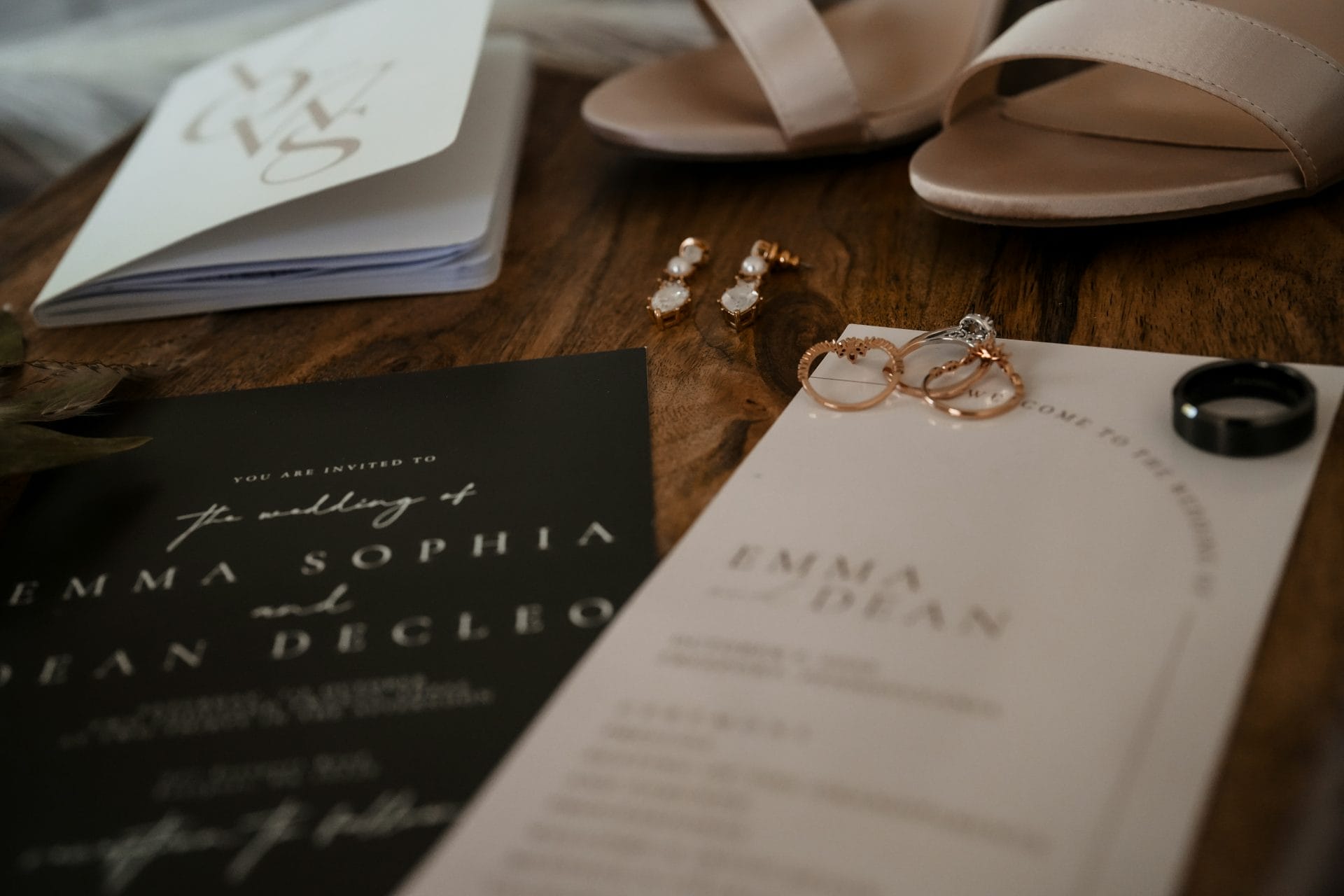 Wedding invitation, vows, rings, and earrings on a wooden table.